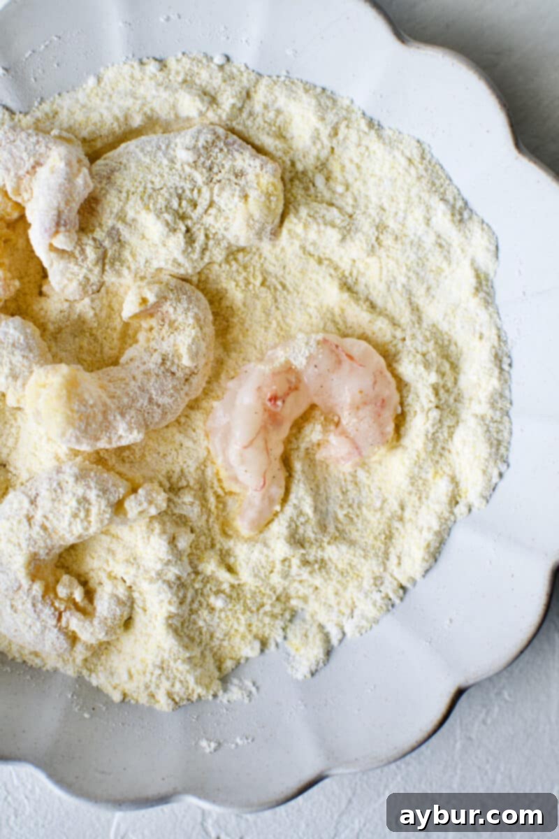 Dredging marinated shrimp in a mixture of flour and cornmeal, preparing them for frying to a crispy coating.