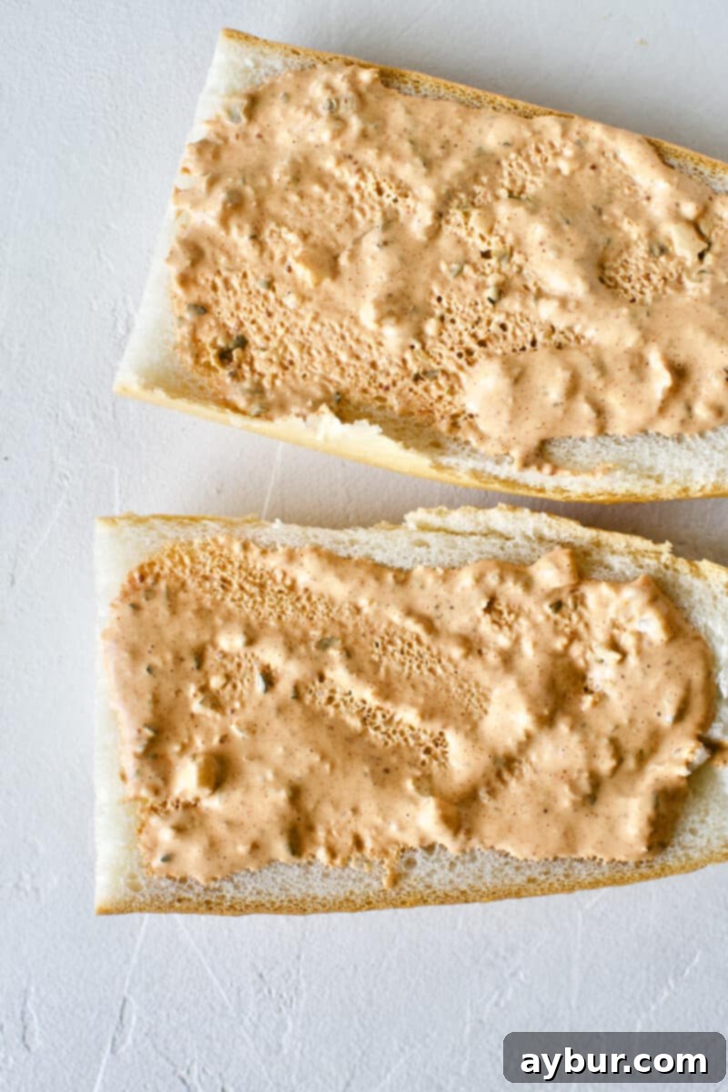 Building a Shrimp Po'boy Sandwich: French bread generously coated with homemade remoulade sauce on both halves, serving as the flavorful base.