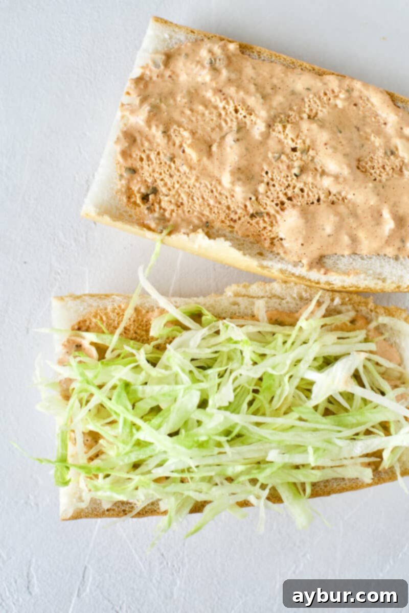 Building a Shrimp Po'boy Sandwich: French bread with remoulade and a layer of crisp shredded lettuce added.