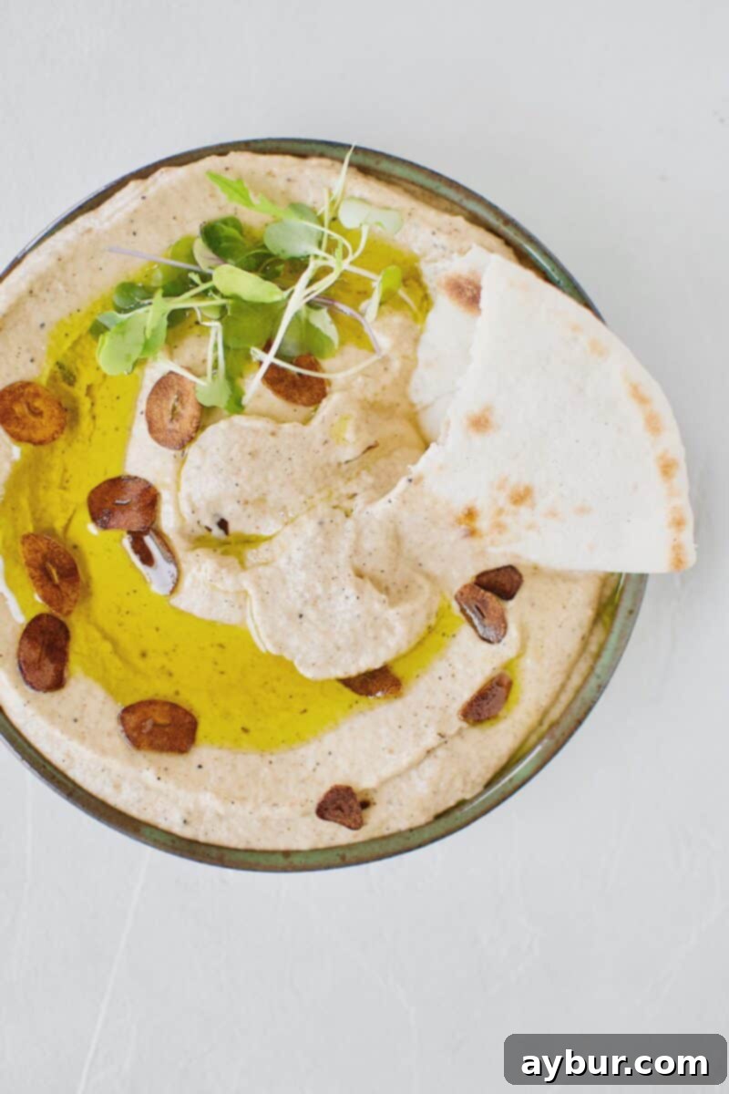Smoky Baba Ghanoush with Golden Garlic 15 A bowl of Baba Ghanoush with Toasted Garlic, garnished and served with a piece of pita bread dipped into it.