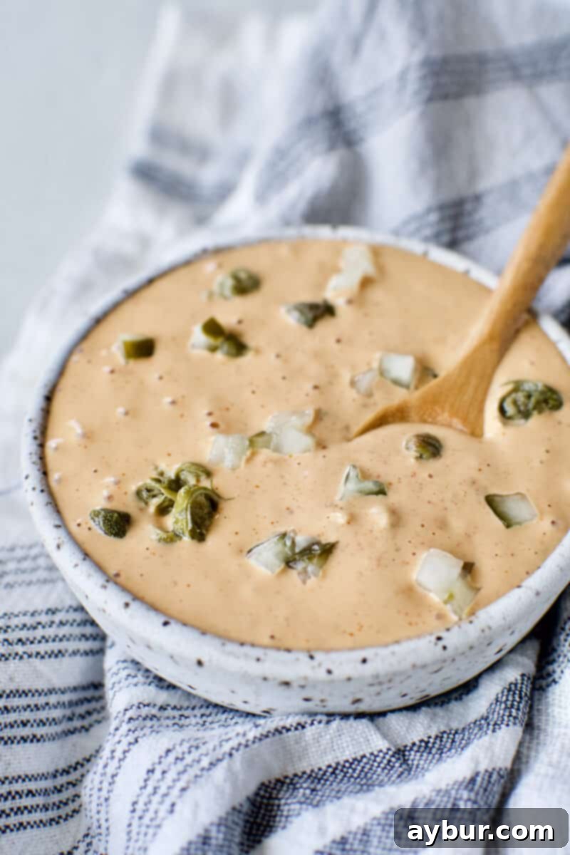 Effortless Remoulade Sauce 4 Easy homemade Remoulade Sauce prepared and served in a bowl, garnished with finely diced dill pickle and caper pieces, showcasing its rich texture and color.