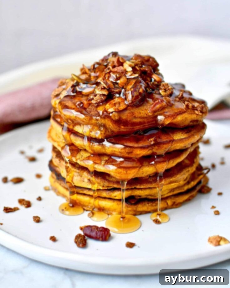 Fluffy Pumpkin Spice Pancakes 5 A stack of Pumpkin Spice Pancakes topped with pumpkin seed granola and maple syrup running down them.
