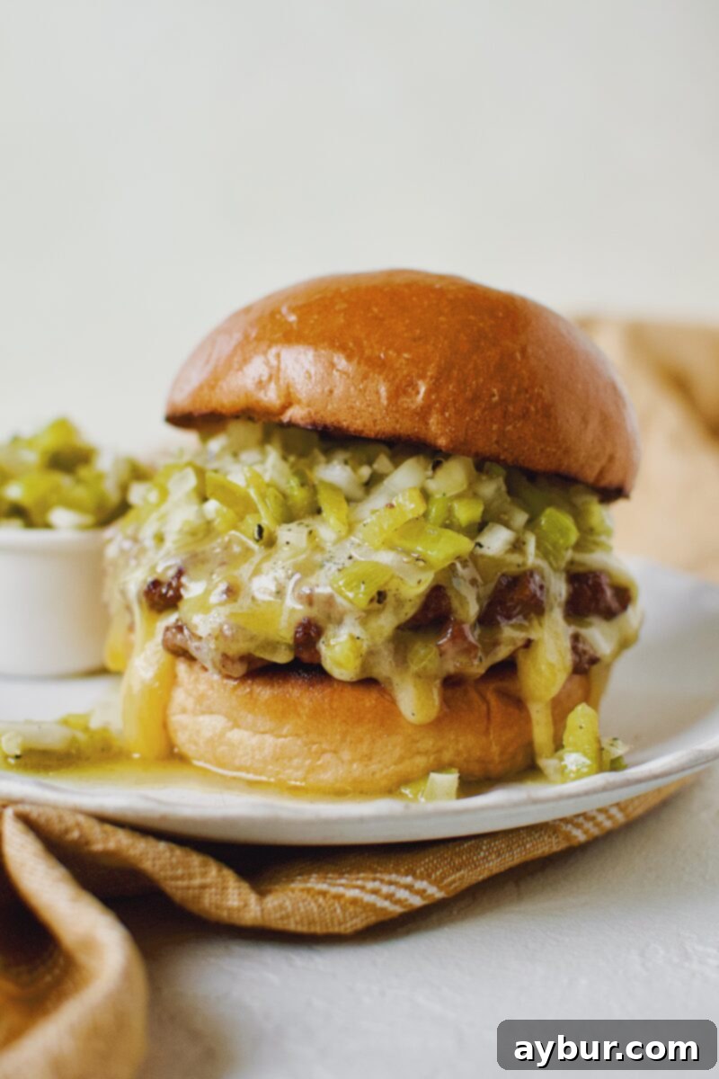 Finished Green Chili Cheeseburger, on a brioche bun, topped with hatch salsa, and cheese melting down the side, presented on a dark plate.