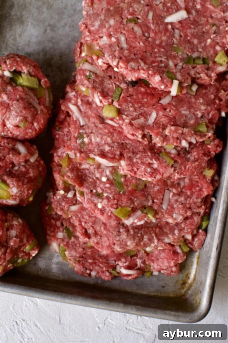 Burgers being patted out thin between two pieces of parchment paper.