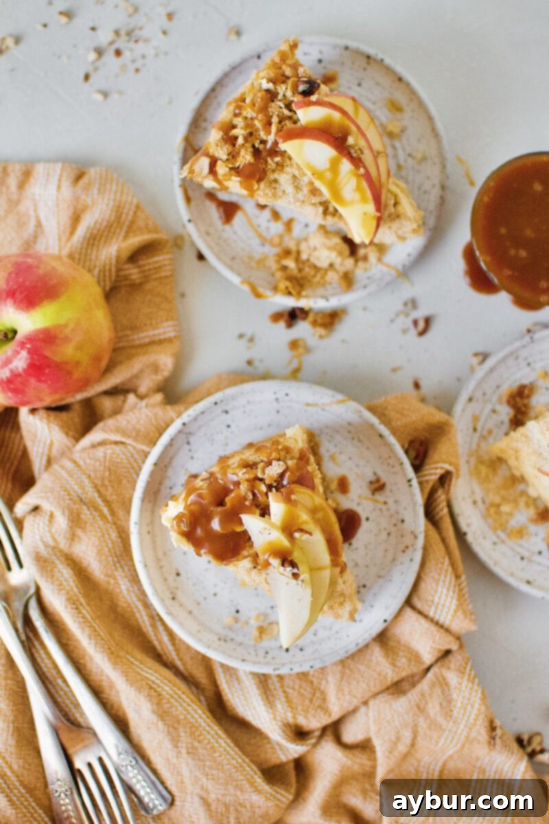 A beautifully presented slice of Caramel Apple Crisp Cheesecake on a white plate, revealing its creamy layers, apple chunks, and crunchy topping.