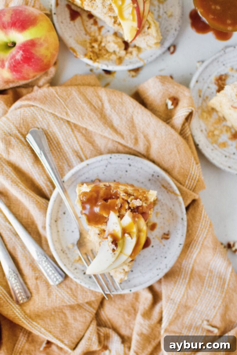 A beautifully presented slice of Caramel Apple Crisp Cheesecake, perfectly showcasing the creamy cheesecake, apple layer, and golden crisp topping.