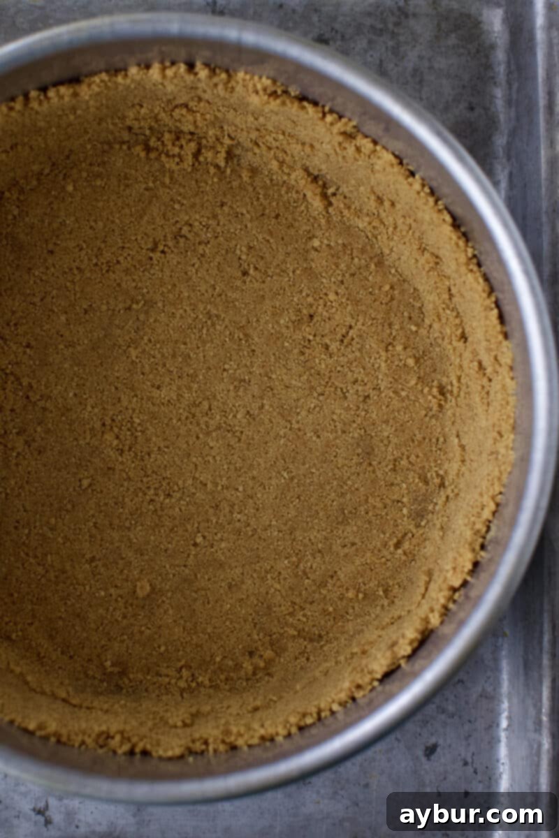 A golden brown graham cracker crust, perfectly pressed into the bottom of an 8-inch cake pan and partially up the sides, freshly baked and cooling.