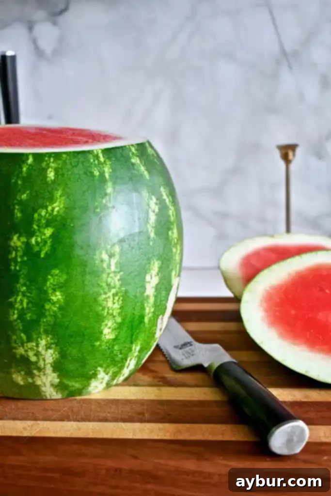 A chef using a serrated knife to carefully slice off the green rind of a vertically standing watermelon