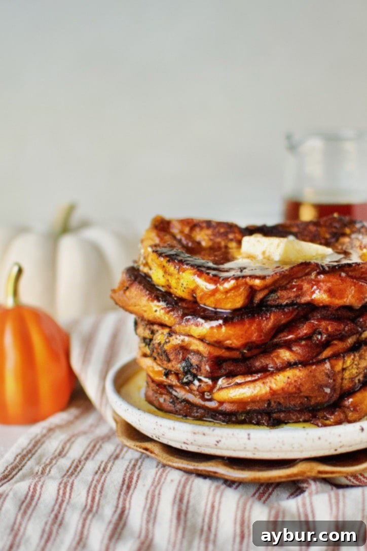 A stack of perfectly cooked Pumpkin French Toast, garnished with a pat of butter, a drizzle of maple syrup, and a sprinkle of pumpkin pie spice, ready to be enjoyed.