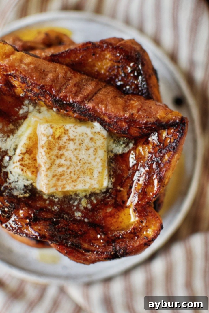 A stack of golden-brown Pumpkin French Toast, artfully topped with a melting pat of butter and a generous drizzle of glistening pure maple syrup, ready to be devoured.