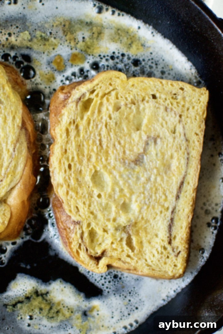 A slice of brioche bread, thoroughly soaked in pumpkin custard, being placed into a cast iron skillet with melted butter and oil.