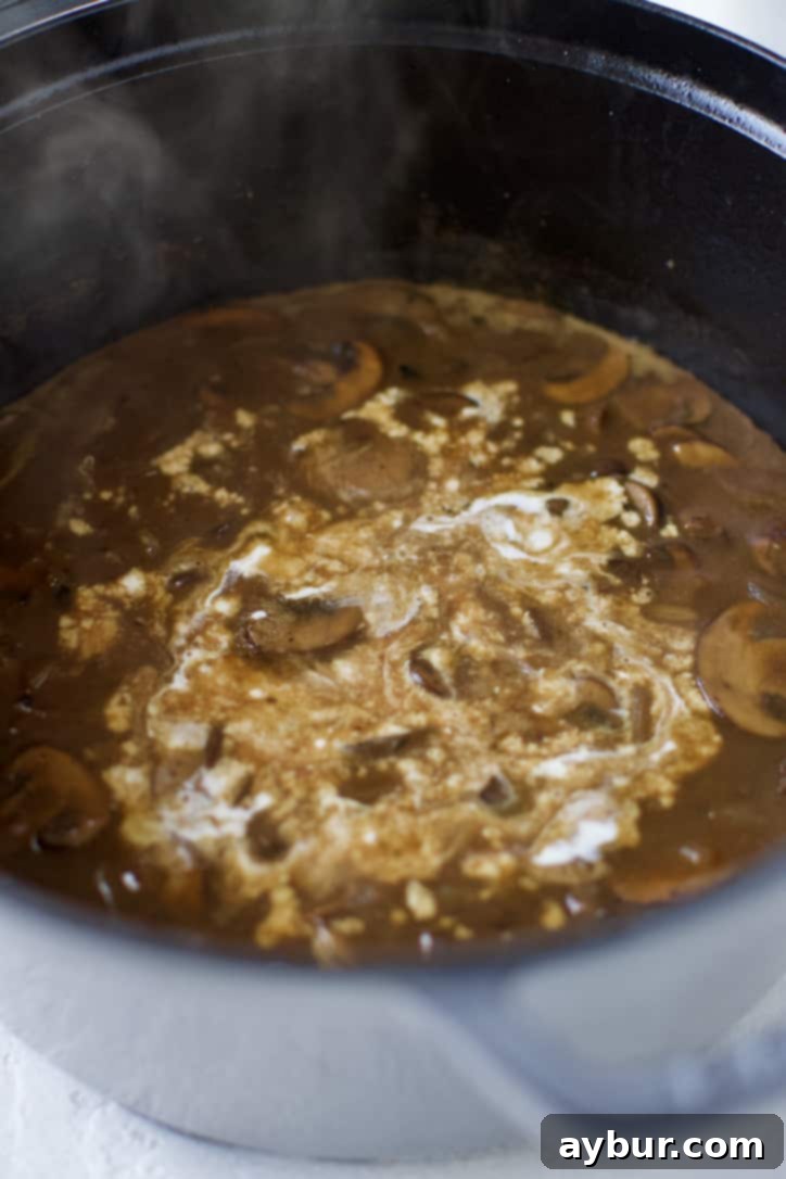 Pouring rich heavy cream into the simmering meatball gravy, completing the luxurious sauce.