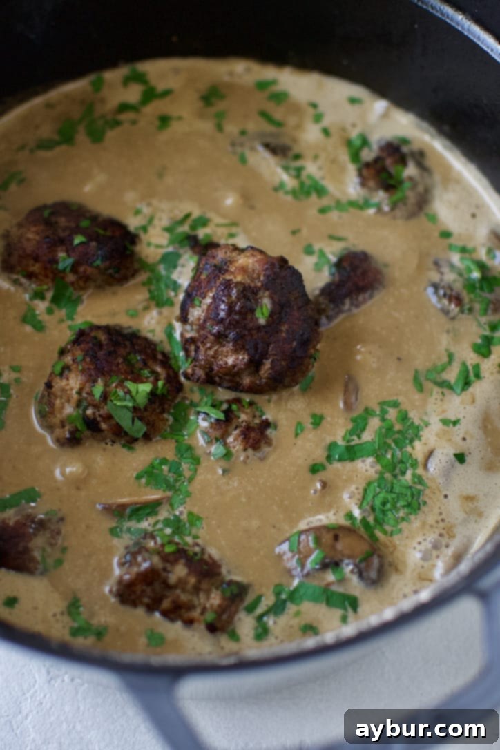Cooked Swedish meatballs being added back to the creamy sauce in the pot to simmer and absorb flavors.