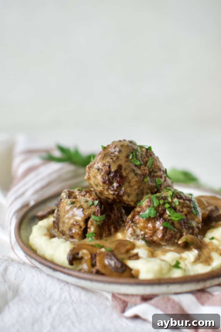 A close-up shot of creamy Easy Swedish Meatballs and mashed potatoes, garnished with fresh herbs, ready to serve.