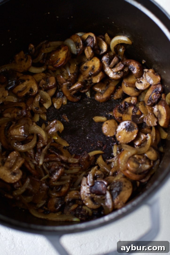 Sliced crimini mushrooms and onions sweating and caramelizing in butter at the bottom of a large pot, creating a flavorful base.