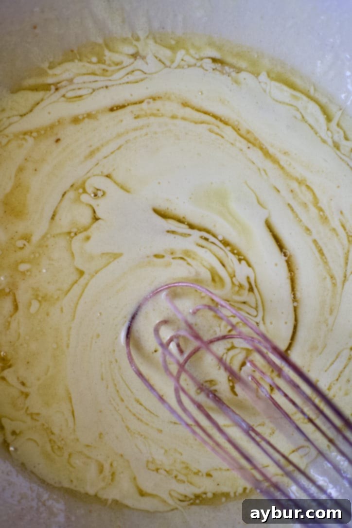 Harvest Apple Cider Donut Cake 6 Carefully whisking warm, brown butter into the fluffy egg and sugar mixture, ensuring even incorporation for rich flavor.