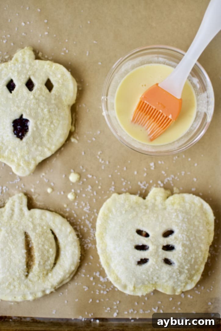 Hand pies being brushed with egg wash and sprinkled with sanding sugar before baking, showcasing careful preparation.