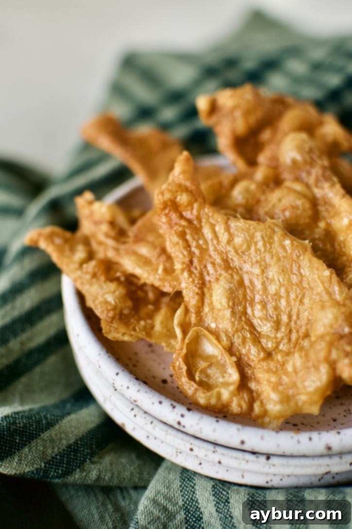 Crispy chicken cracklings removed from the oven and placed on a paper towel-lined plate, with rendered chicken fat in the pan.