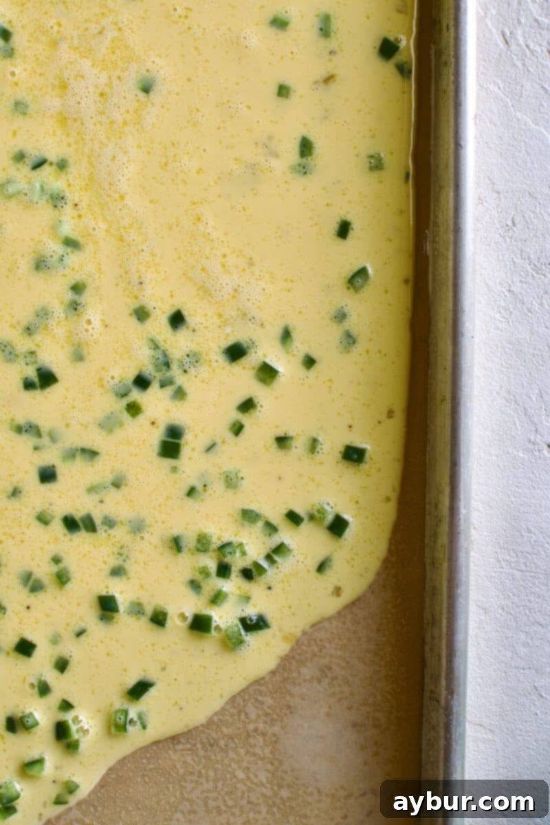 Wholesome Breakfast Sandwich 8 Pouring egg mixture onto a parchment-lined baking sheet.