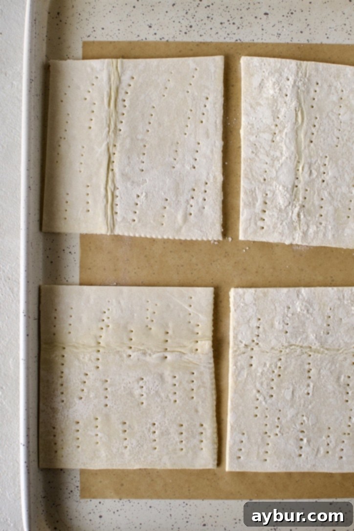 Beef Pot Pie 10 Puff pastry squares, carefully docked with a fork, laying on a baking sheet, ready for cheese and baking.