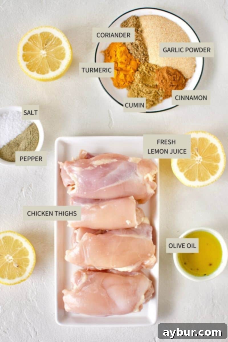A collection of fresh ingredients laid out on a table, including raw chicken thighs, various spices in small bowls, fresh lemons, and olive oil, ready for making Chicken Shawarma.