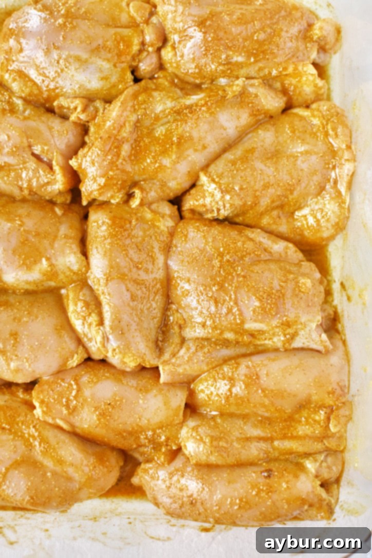 Raw chicken thighs soaking in a vibrant yellow-orange marinade in a glass bowl, ready for absorption of Middle Eastern spices.