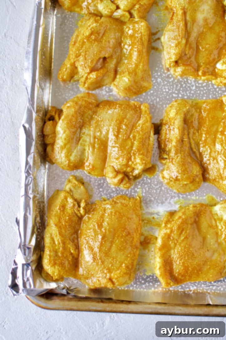 Marinated chicken thighs neatly arranged on a foil-lined, greased baking sheet, ready to be broiled for Chicken Shawarma.