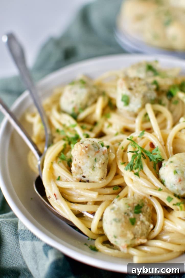 Close-up of Italian Shrimp Balls served in a white bowl over cooked bucatini pasta, garnished with fresh parsley.
