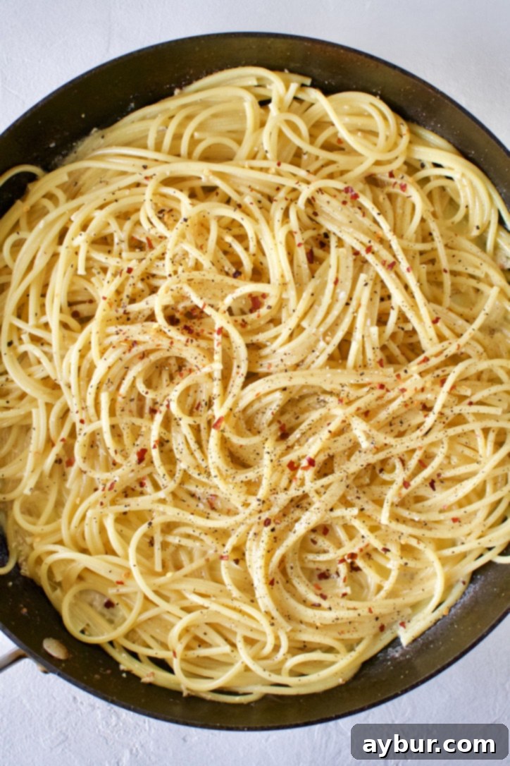 Cooked bucatini pasta being tossed in a skillet with the seasoned butter and garlic from cooking the shrimp balls.