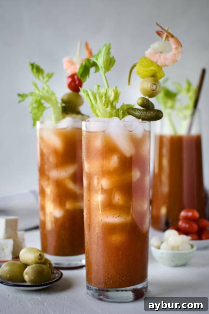 An array of beautifully presented Bloody Marys, garnished elaborately with a wide variety of toppings including bacon, shrimp, olives, pickles, and peppers, arranged around a large pitcher of the vibrant red cocktail mix.
