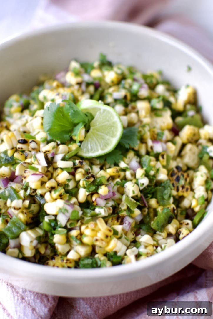 Smoky Sweet Corn and Pepper Salsa 2 Vibrant Roasted Chili-Corn Salsa in a bowl, garnished with a fresh lime slice and cilantro sprigs, ready to be enjoyed.