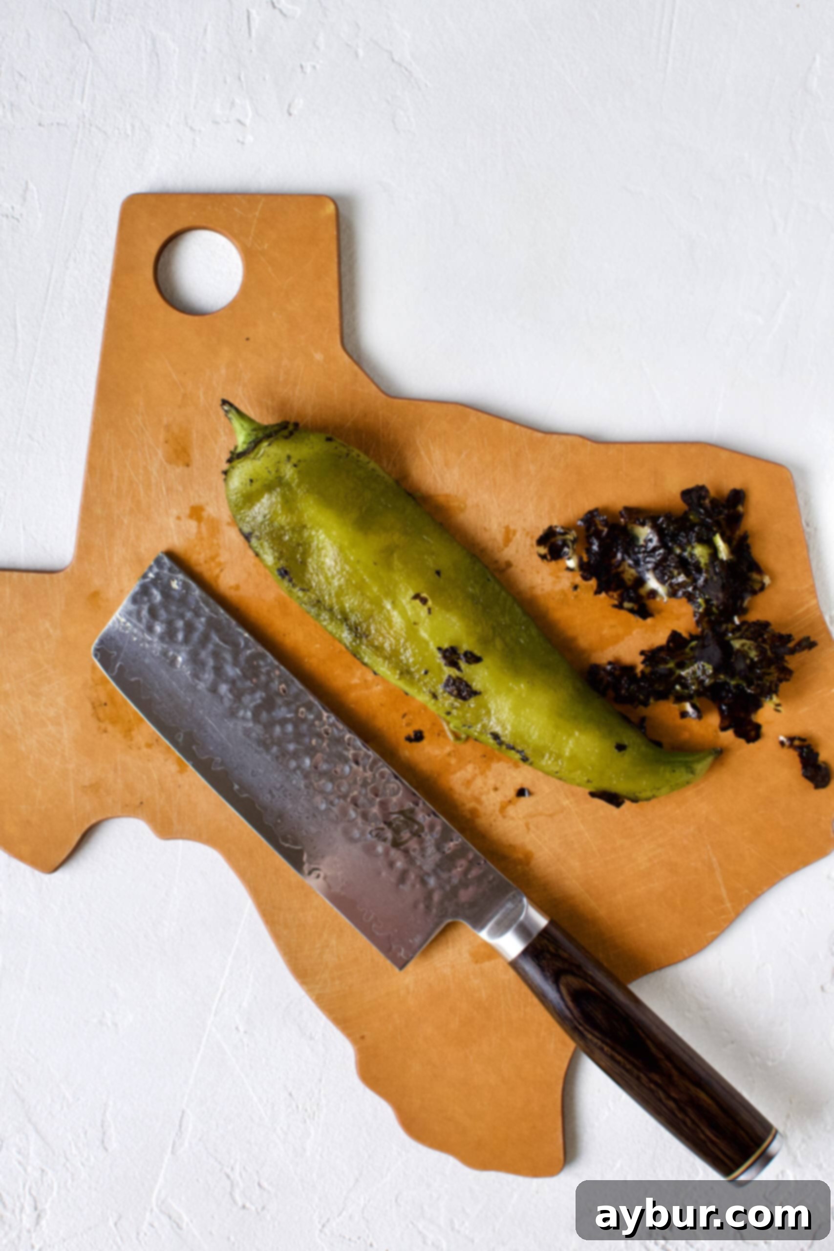 Smoky Sweet Corn and Pepper Salsa 6 A hand using the back of a knife to scrape off the charred, blistered skin from a roasted hatch chile, revealing the soft green flesh beneath.