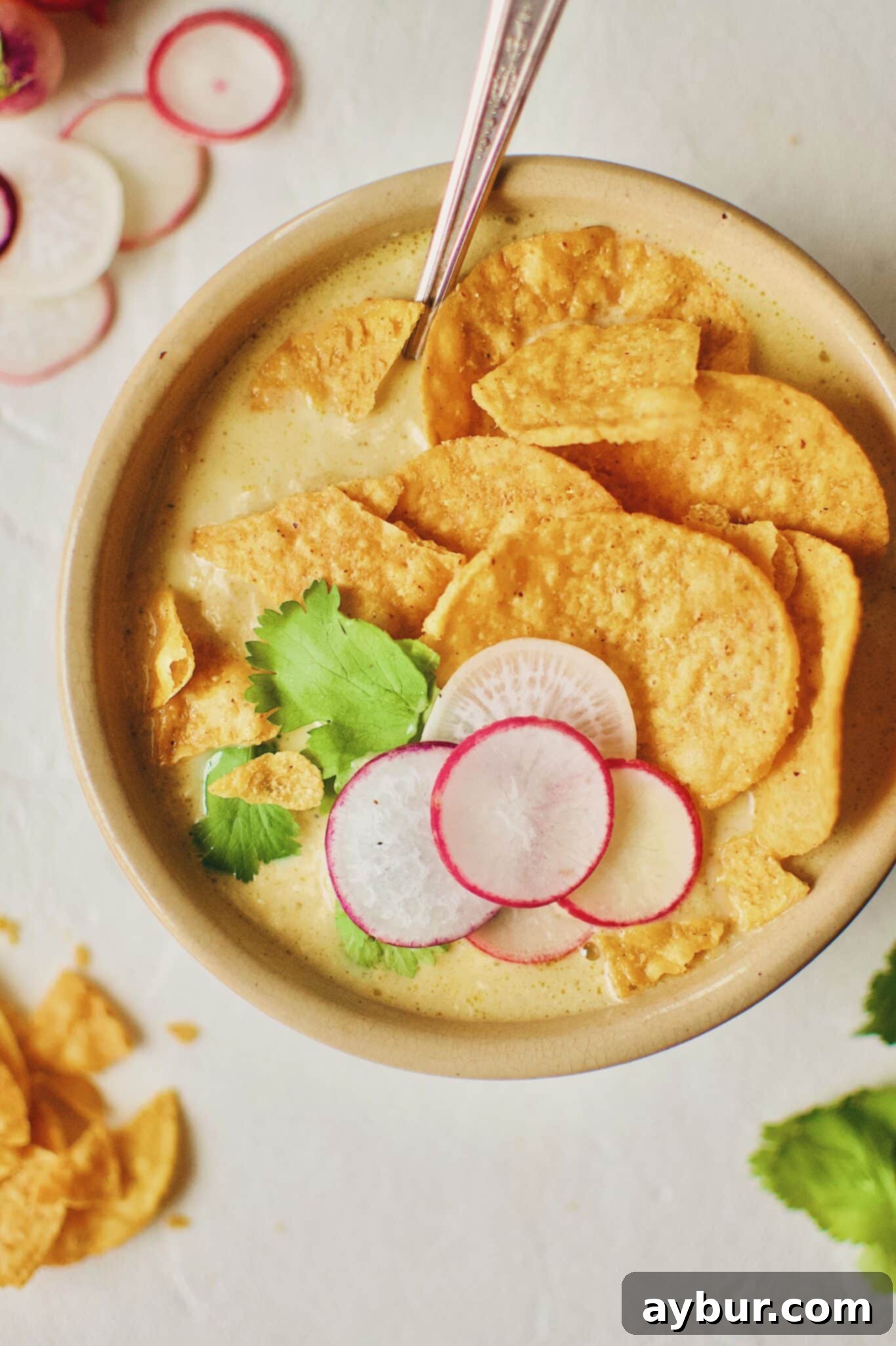A bowl of Joanna Gaines Creamy Chicken Poblano Soup garnished with fresh radishes and cilantro, prepared by KendellKreations.com.