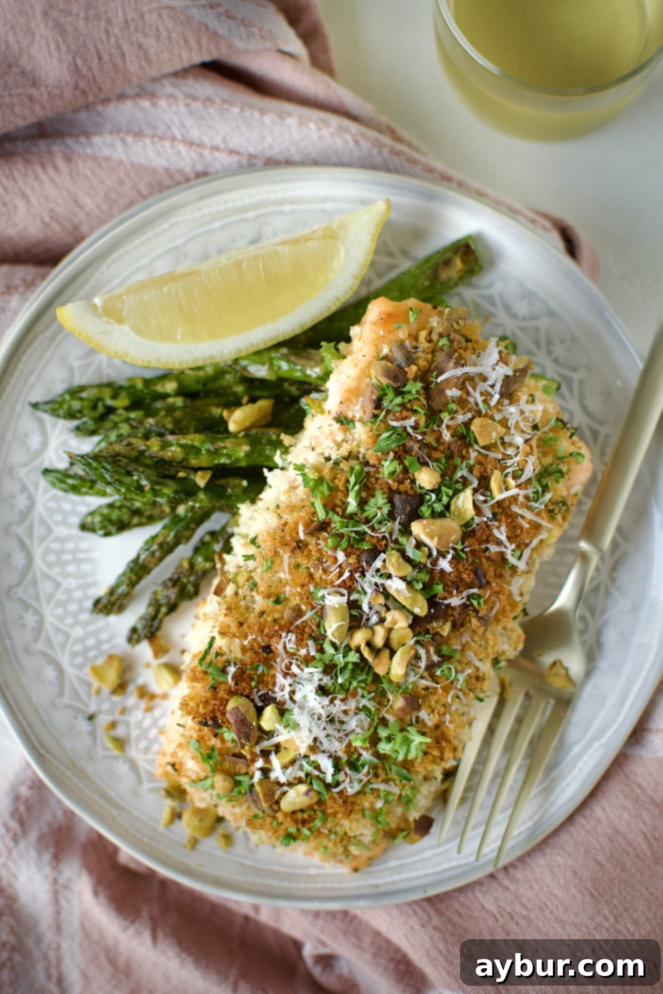 Crisp Pistachio Salmon 12 Pistachio Crusted Salmon on a plate with some grilled asparagus and a lemon wedge. Ready to eat.