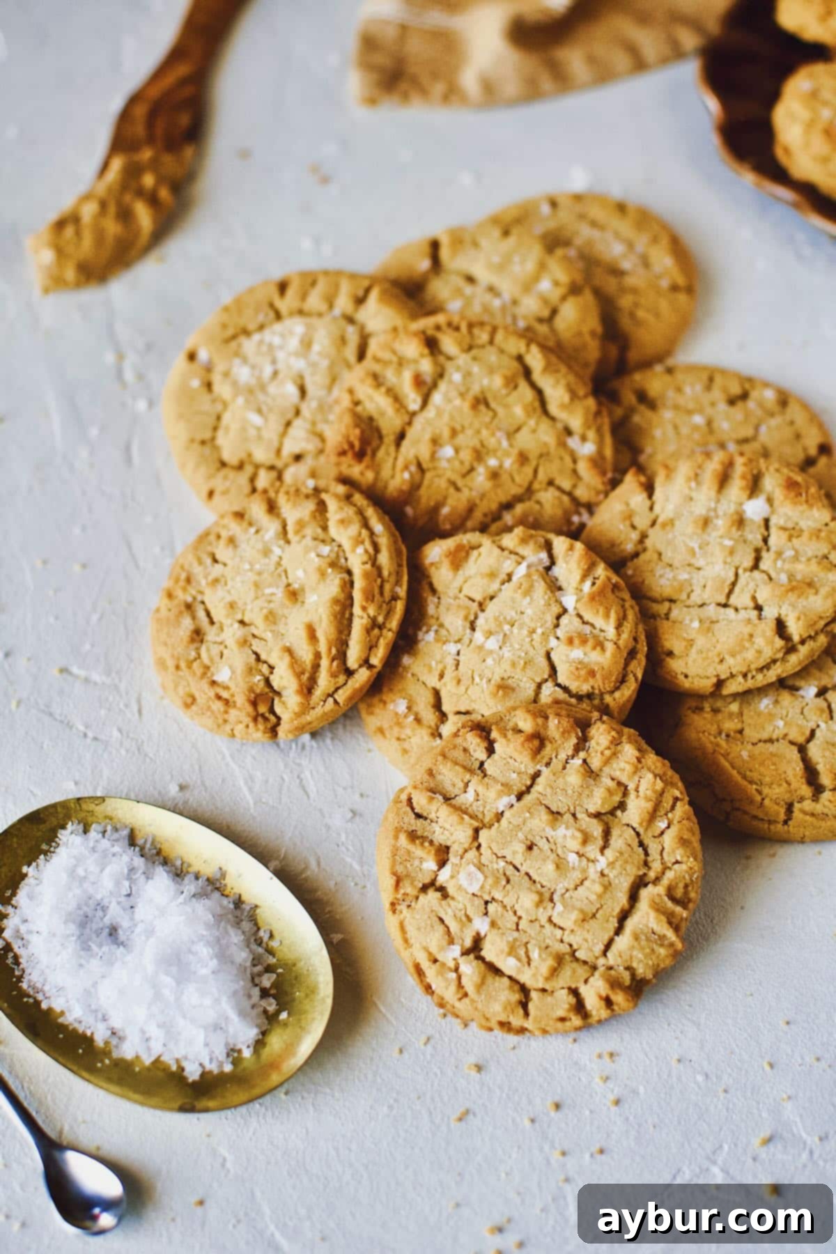 Peanut Butter Crunch Cookies 3 A close-up of delicious crunchy peanut butter cookies, sprinkled with flakey sea salt, piled high on a rustic kitchen counter.