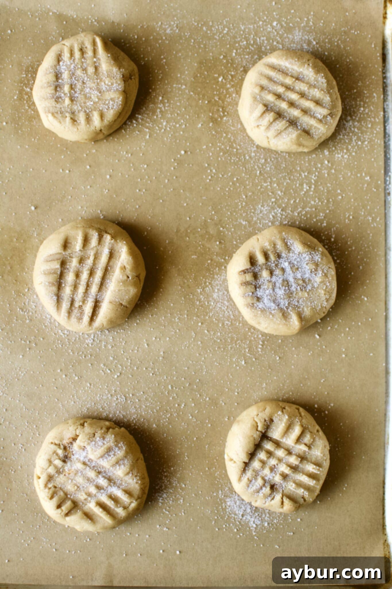 Peanut Butter Crunch Cookies 10 Perfectly portioned cookie dough balls, each adorned with the classic cross-hatch pattern, are arranged on a baking sheet, eagerly awaiting their time in the oven.