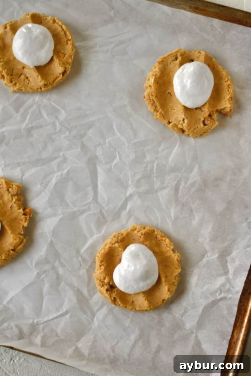 A piping bag precisely adding luscious marshmallow cream into the center of each flattened peanut butter cookie dough.