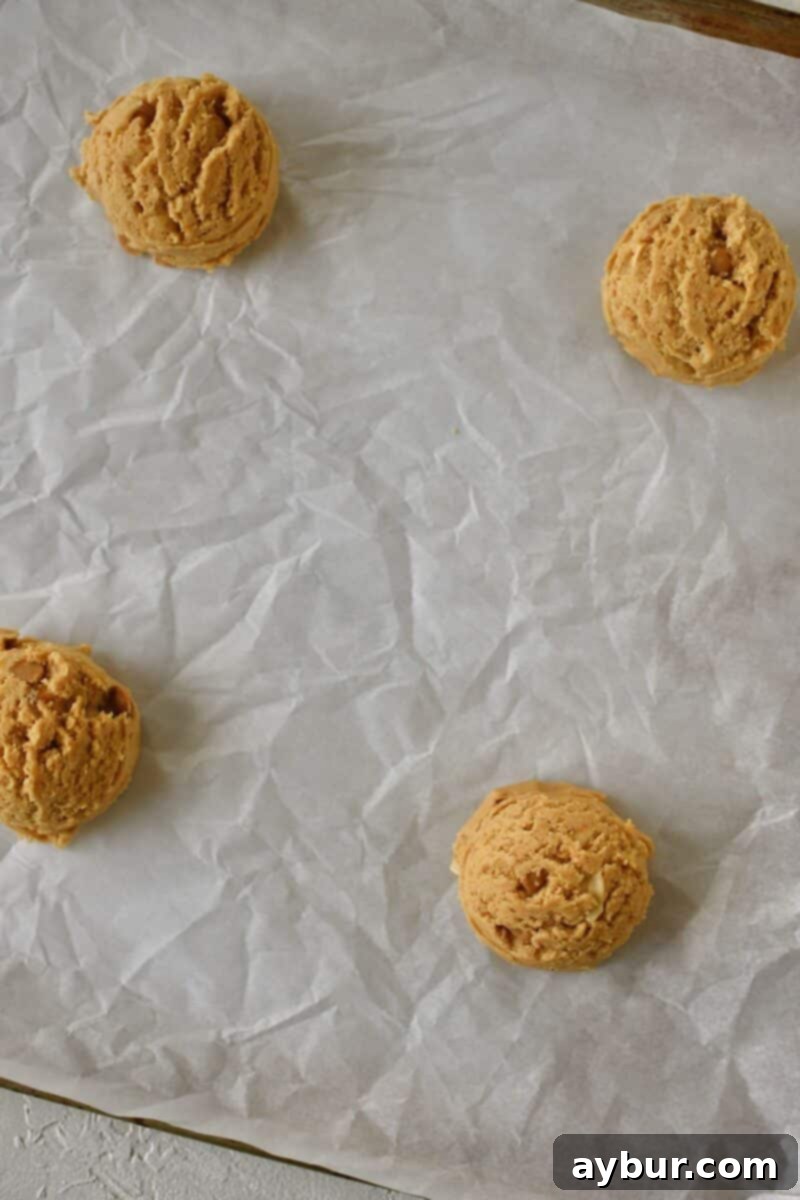 Uniformly portioned cookie dough balls resting on a parchment-lined baking sheet, ready for the next step.