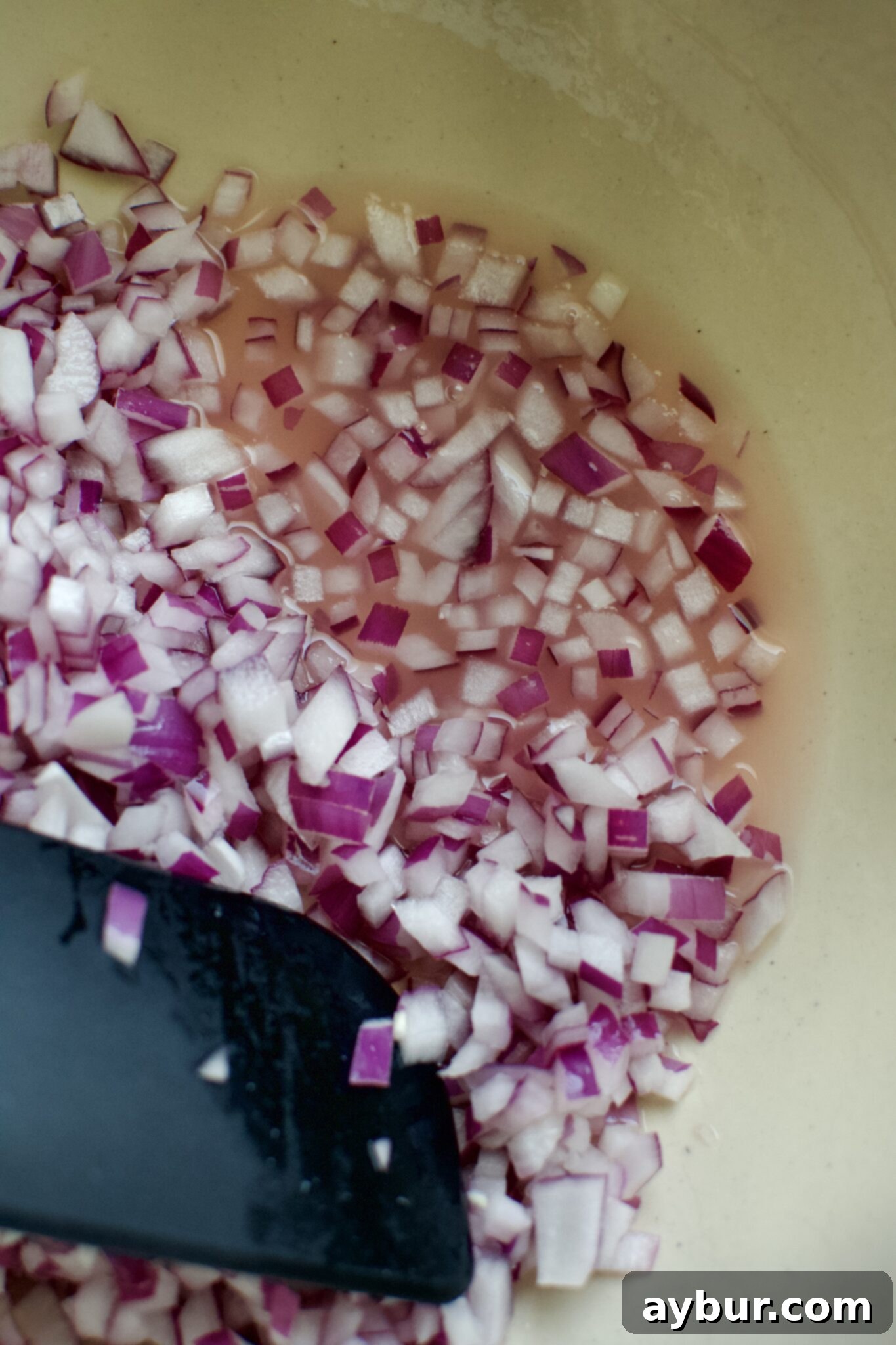 Finely diced red onions seasoned with lime juice and salt in the bottom of a large bowl.