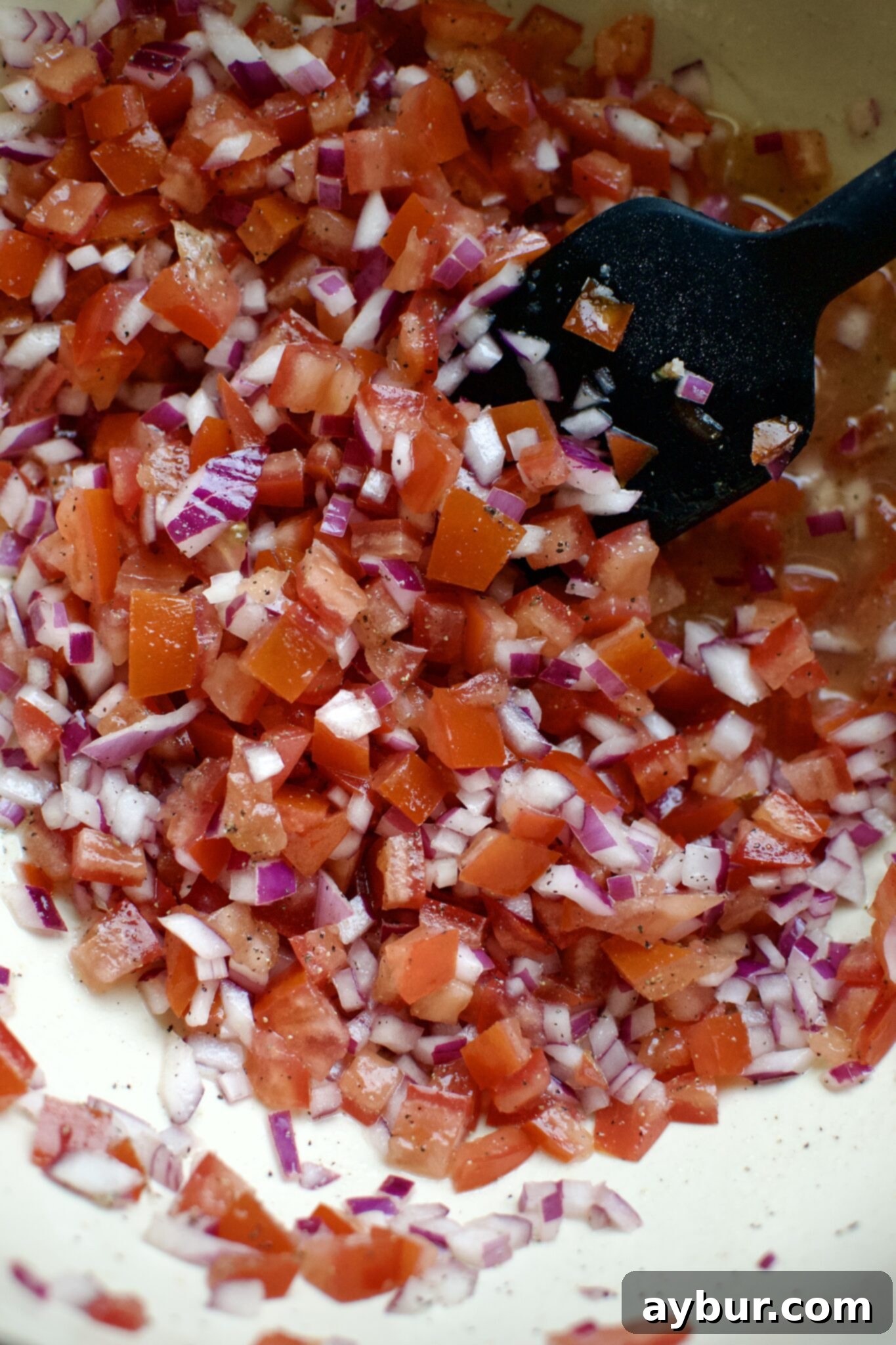 Diced red onions and tomatoes, seasoned with salt, pepper, and lime juice, at the bottom of a large mixing bowl.