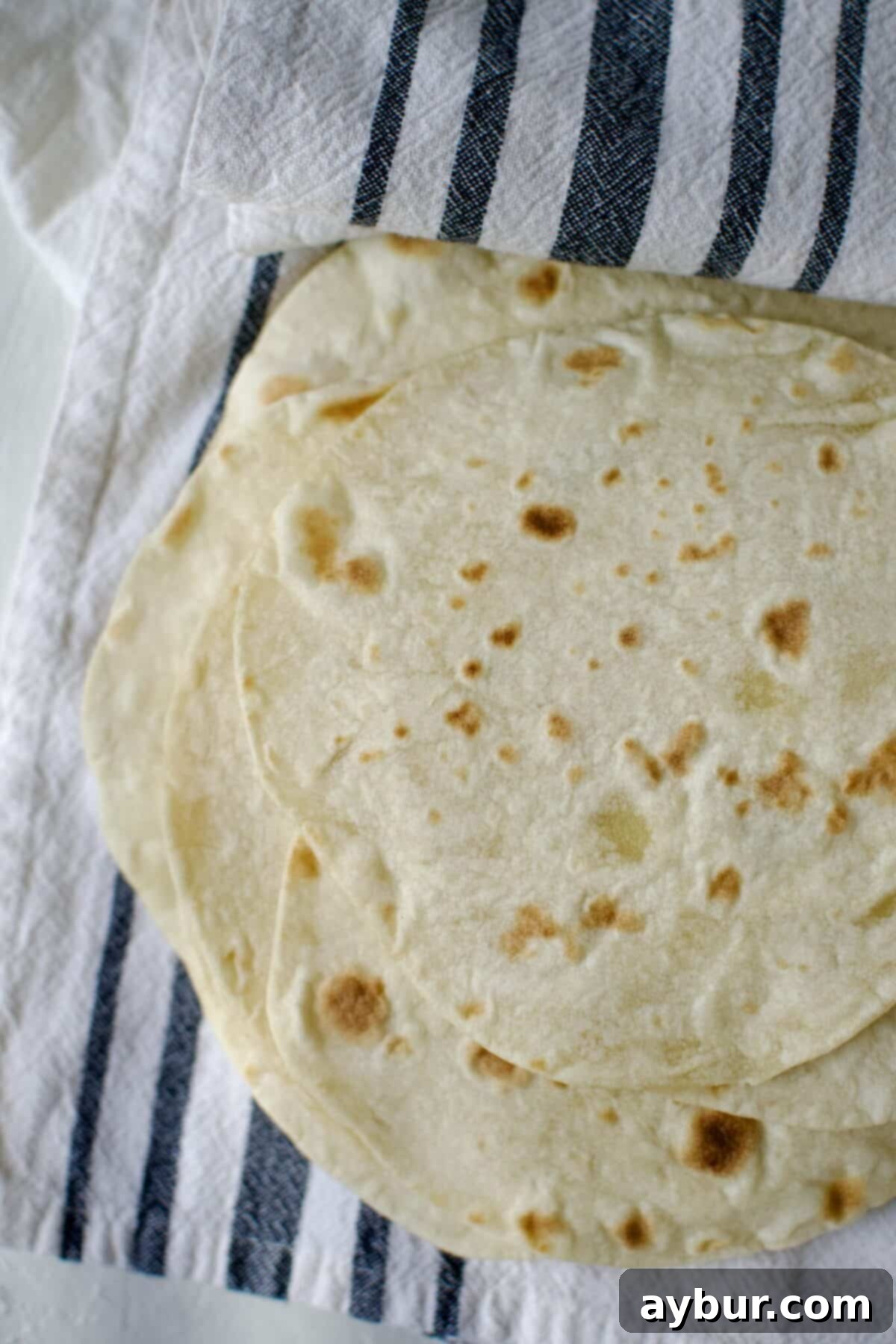 Soft, pliable homemade flour tortillas stacked and kept warm under a kitchen towel, ready for your next meal.