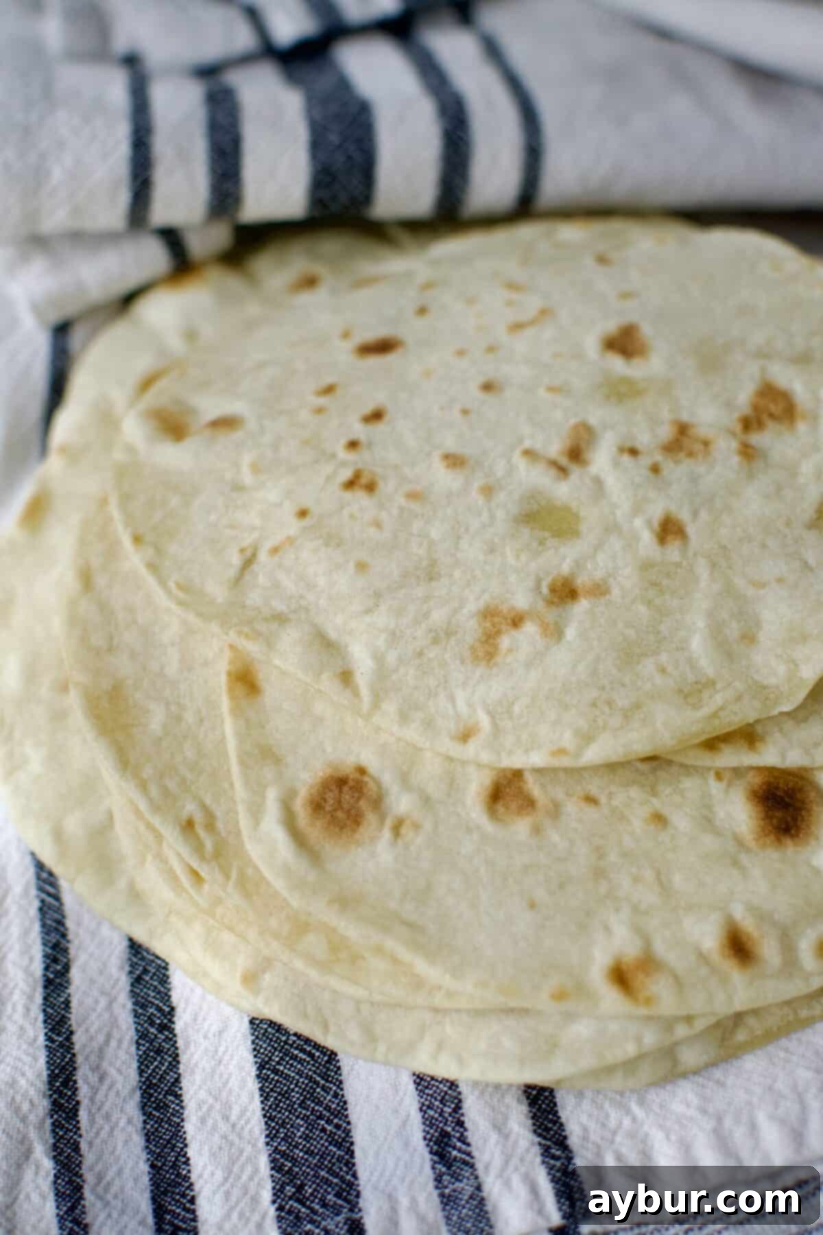 Freshly cooked homemade flour tortillas stacked on a plate, steamy and ready to serve.