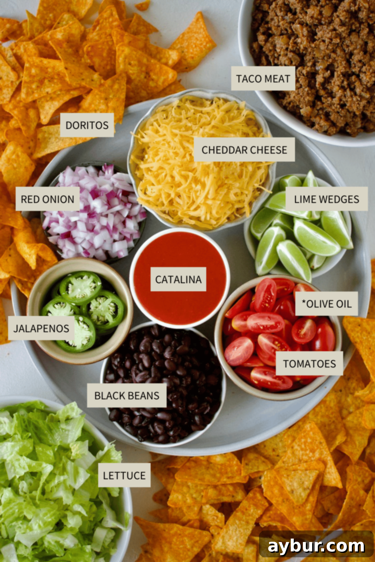 A colorful display of fresh ingredients needed to make Doritos Taco Salad, including ground beef, lettuce, tomatoes, onions, cheese, and Doritos.