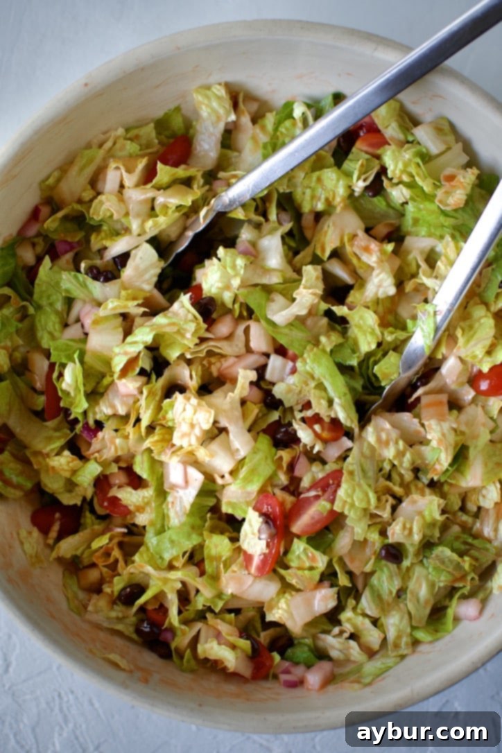 Assortment of fresh ingredients for taco salad being prepped: chopped lettuce, grape tomatoes, and rinsed black beans.