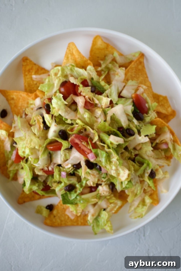 Adding a generous layer of fresh lettuce and vegetable mixture over the Doritos base.
