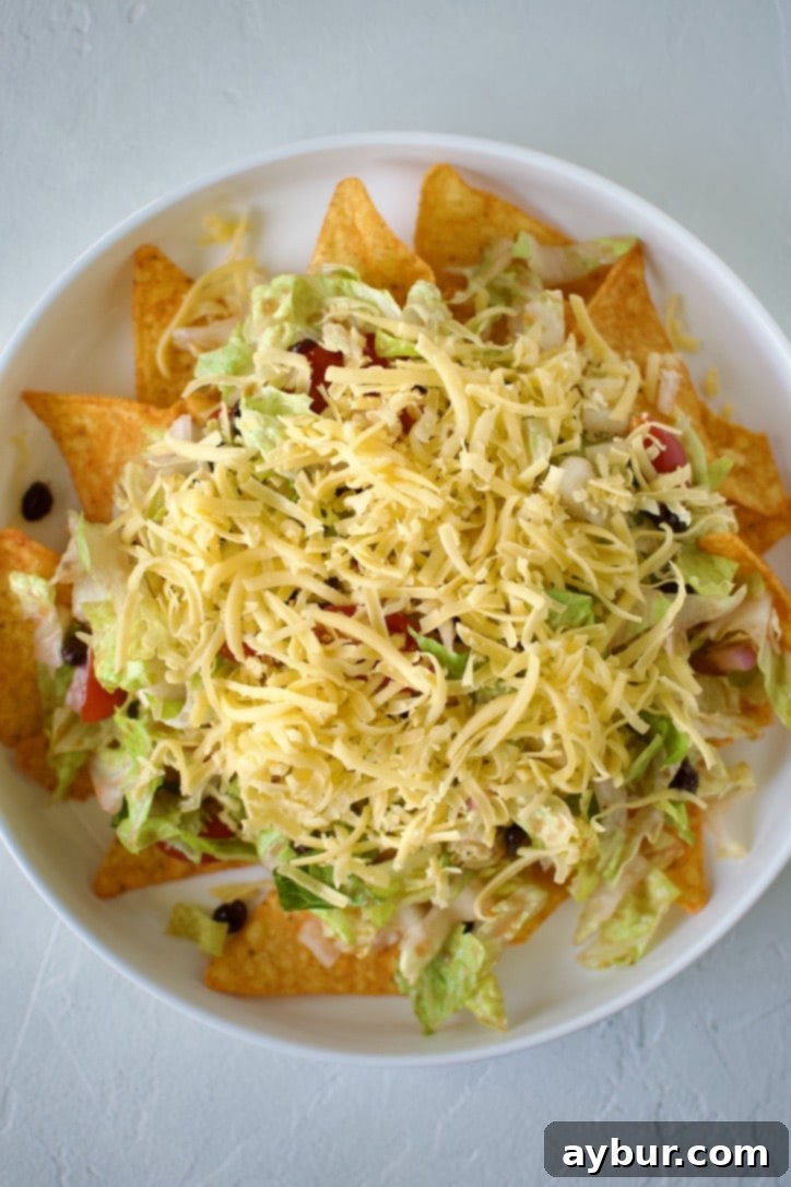 Spoonfuls of seasoned ground beef being added to the layered taco salad.