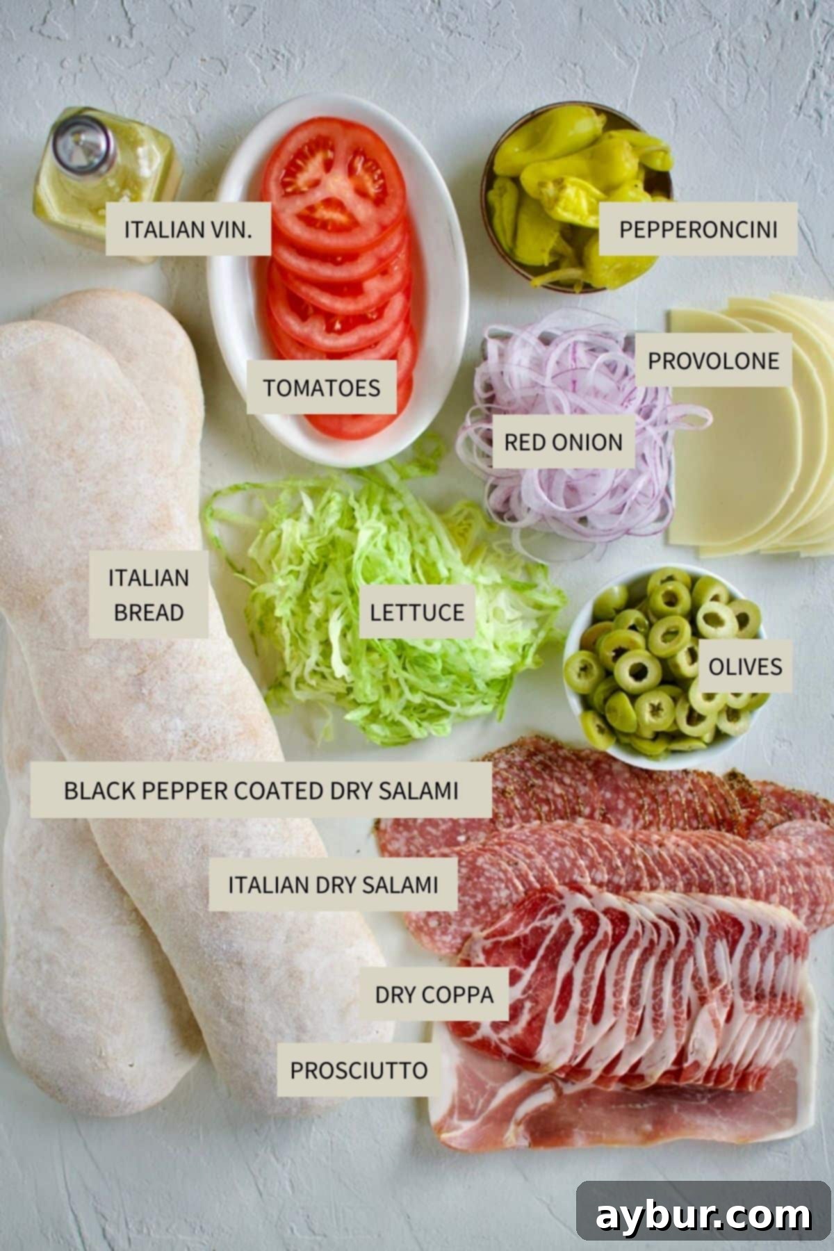 Ingredients laid out for making the Italian Subs Recipe, including bread, meats, cheese, and vegetables.
