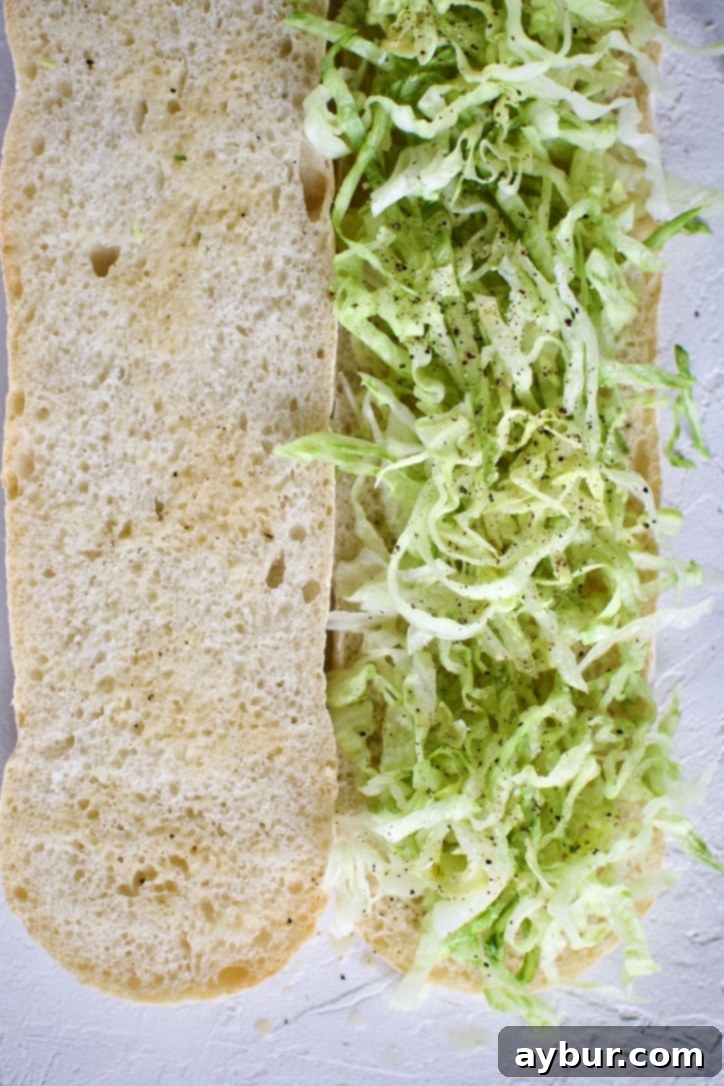 The first step of making Italian Subs: open the bread, add a layer of shredded lettuce, and drench both sides with Italian vinaigrette.
