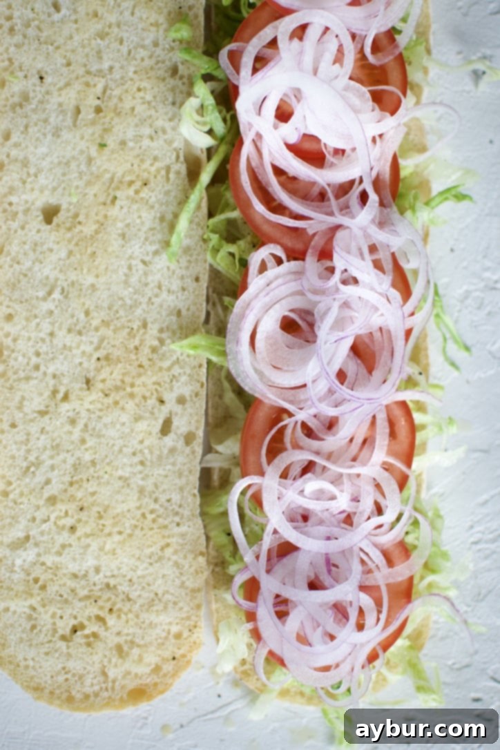 Layering thinly sliced red onions onto the Italian Sub.