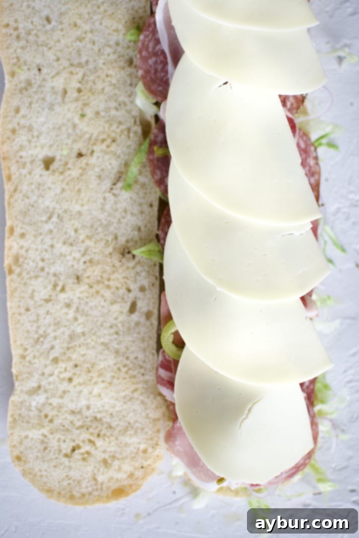 Placing provolone cheese slices as the final layer on the Italian Sub.